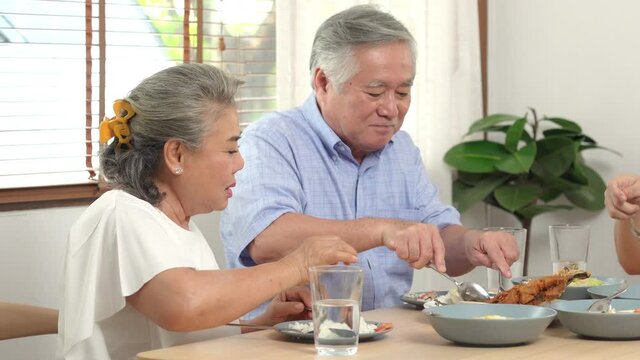 Asian family having dinner together at home. Smiling adult couple with senior parents enjoy eating and sharing thai food on dining table. Happy family spending time together on weekend vacation.