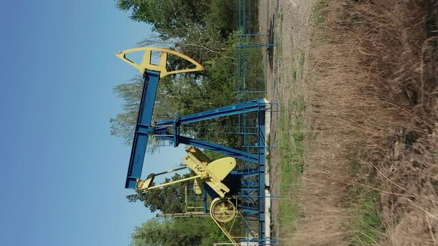 Vertical Shot Of A Working Oil Pumpjack In An Oilfield At Daylight. dolly-in