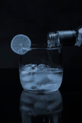 Drink of beverage served in a glass tumbler,
Glass tumbler with ice and a slice of lemon with drink served with a bottle. Close up image in white with black