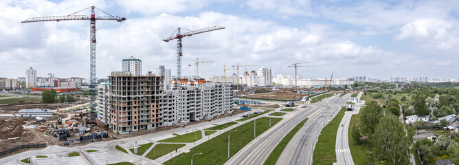 panoramic aerial view of city construction site with buildings and cranes under blue cloudy sky