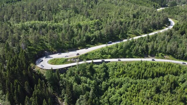 Cars driving down evergreen hillside in cury Norway road - Aerial of road with cars driving downhill before revealing river close by - F&oslash;rde E39 road