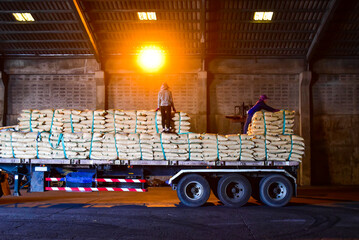 Warehouse intake, workers unloading bags of sugar cargo using forklift from truck to stack inside a...