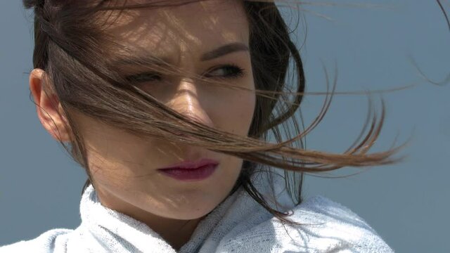 The wind moves the woman's hair. A young woman is standing on the beach during a storm wrapped in a towel against the cold wind. A day at the seaside.