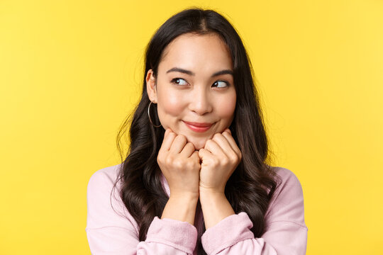 People emotions, lifestyle leisure and beauty concept. Silly dreamy asian girl have interesting idea in mind, imaging something as peeking left and smiling, scheming plan, yellow background