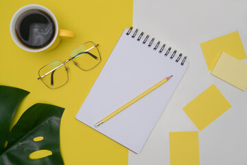 Notebook, coffee cup, sticky notes and glasses on yellow background.