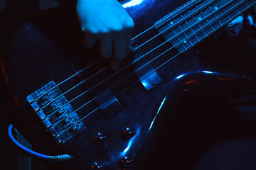 The bass player plays on black five-string bass guitar in the spotlight. Selective focus - obrazy, fototapety, plakaty