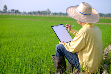A farmer wearing a yellow long-sleeved shirt is sitting in a field holding a note board with blank paper.
