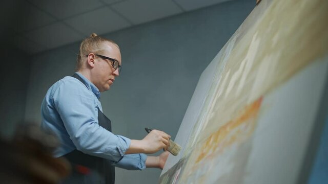 Creative person at work, a talented adult man artist covers the canvas with beige oil paint, draws the modern abstract picture, 4k slow motion.