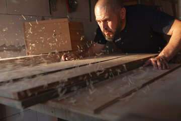 A carpenter blows sawdust off a board