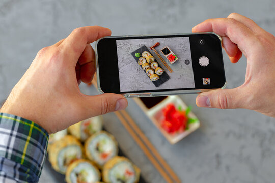 Male hands holding smartphone and taking a photo of sushi roll on gray background