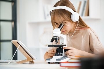 Young girl using microscope during online lesson education at home