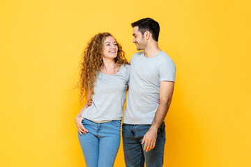 Young happy interracial millennial couple holding and looking each other in the eyes in isolated yellow studio background - obrazy, fototapety, plakaty