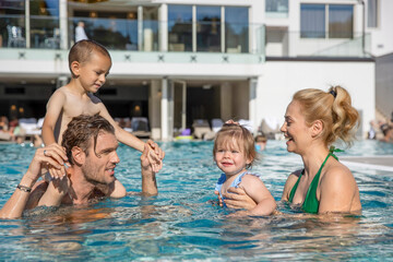 Fototapeta na wymiar Happy family, parents playing with the kids, mother and daughter in the swimming pool