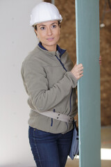 female builder carrying sheet of plasterboard