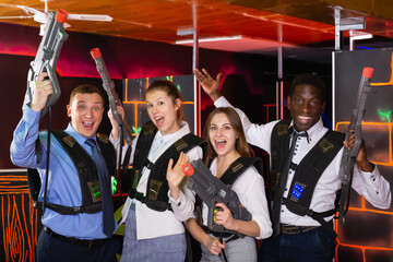 Group of jolly co-workers holding laser guns and posing at laser tag room