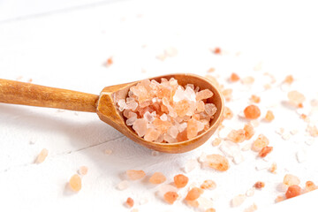 Fototapeta na wymiar Wooden spoon with large crystals of pink himalayan salt on a white wooden background. Himalayan salt for cooking, medicine and cosmetology.
