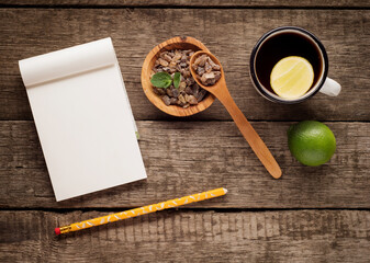 old enamel cup of tea with brown sugar mint and wooden spoon on rustic wooden background with notepad