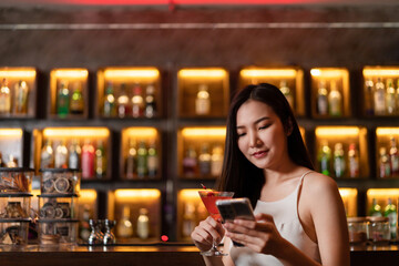 Nightlife concept a sexy girl with smiling face checking messages in her smartphone with a vivid pink champaign in her hand