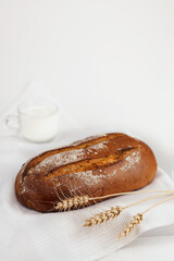 The bread is lying on a white napkin. Next to him are wheat ears, a mug of milk. Selective focus.