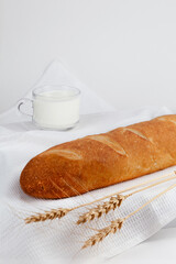 The bread is lying on a white napkin. Next to him are wheat ears, a mug of milk. Selective focus.