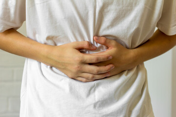 The young man holds his stomach with his hands, experiencing pain and spasms.