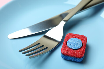 Plate with cutlery and dishwashing tablet, close up