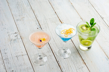 Three ice cold refreshing cocktails on white wooden background.