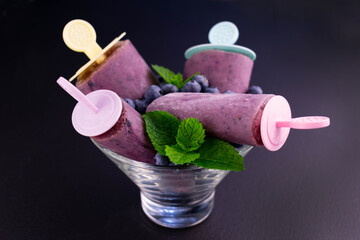 Homemade blueberry ice cream in a glass bowl on a black background.
View from above.