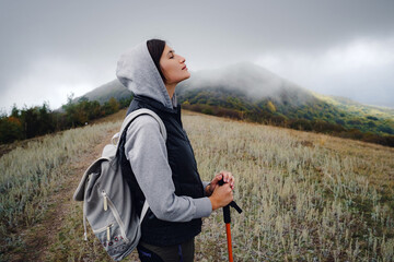 Asian travel woman stands by the mountain. Cold weather, fog on the hills. Autumn hike. The beginning of the autumn season. Beautiful foggy weather