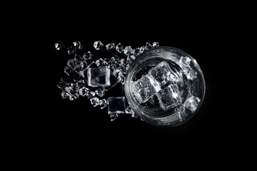 A transparent glass beaker with a colorless liquid ice cubes floating in it and scattered on the...