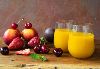 Refreshing sunny summer cocktail of yellow mango and passion fruit on a wooden table with fresh berries - cherries, strawberries, passion fruit, and nectarine. Two glasses of drink
