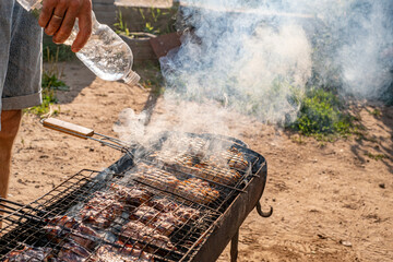 the meat is cooked on a wire rack, the hand pours water from a bottle on the meat