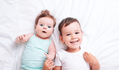 happy little brother hugs his little sister lying on a white blanket