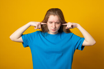 Girl covering her ears with hands for not to hear anything. Photo of young girl dressed in casual clothes on yellow background.