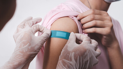 Close up adhesive bandage on woman arm after injection vaccine, medical doctor putting plaster while rubber protective gloves.