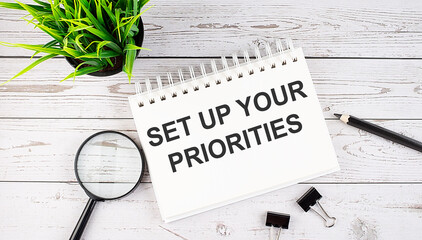SET UP YOUR PRIORITIES text concept write on notebook with office tools on the wooden background