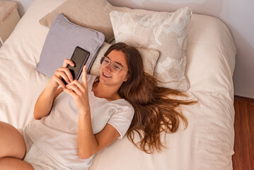 Young latin woman with mobile phone lying in the bed