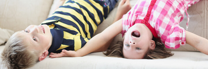 Little boy and girl lying on couch upside down at home