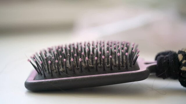 Black and pink hairbrush lies on table with hair band for pony tail or braid fixed on handle after girl brushes closeup