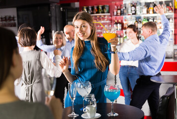 Portrait of smiling girl drinking cocktail and dancing on corporate party