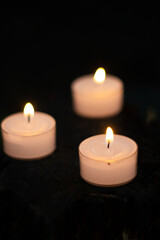Fototapeta na wymiar 3 small burning candles close up shot, shallow depth of field, dark background