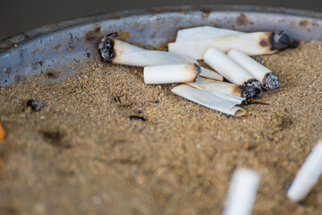 Cigarette butts in the sand on the trash.
