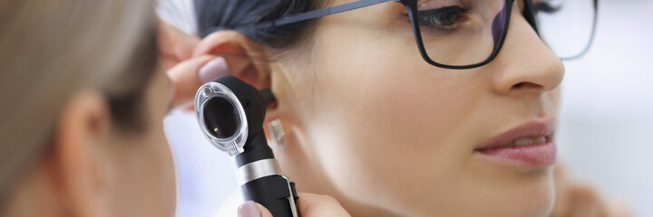 Doctor laryngologist examining ear of female patient with glasses using otoscope