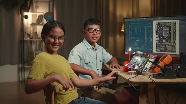It Boy And Girl Are Working With Desktop Computer And Mainboard In Home, Display Showing Cad Software. They Turn And Warmly Smiles Into The Camera, Genius Children Concept
