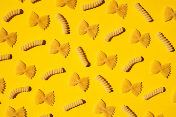 Uncooked curly pasta pattern on yellow background. Traditional dry raw macaroni pattern. Nobody