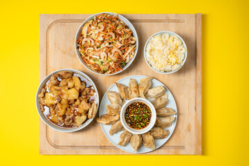 Colorful palette of asian take away food - prawn salad, sweet crunchy chicken, rice and fried dumplings on wooden background