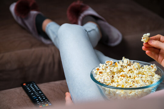 Close Up Of Hand Waking Popcorn From A Bowl While Watching TV. Person Sitting In Comfortable Couch And Watching Home Cinema In The Dark.