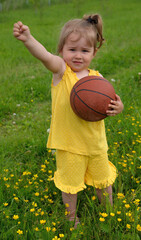 Little girl in yellow suit plays ball on lawn