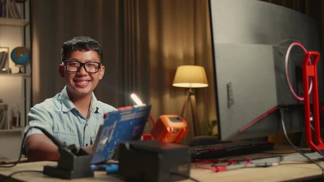It Asian Boy Is Working With Desktop Computer And Mainboard In Home. He Turns And Warmly Smiles Into The Camera, Genius Children Concept

