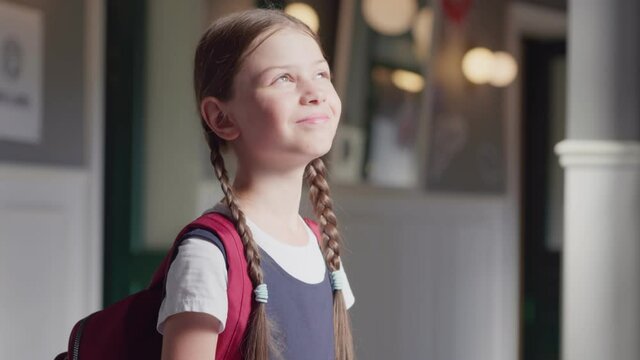 Portrait of happy schoolgirl standing near window in school corridor enjoying sunshine